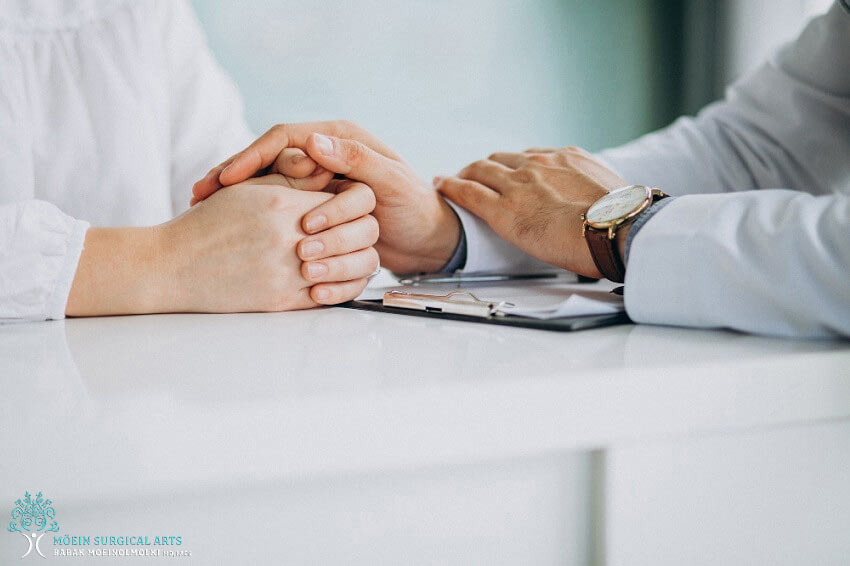 A doctor and a patient holding hands at a desk.