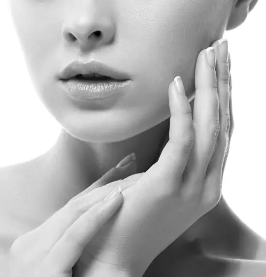 Close-up of a person's lower face and hands touching their cheek, showcasing smooth skin and manicured nails in a black and white image; perfect for highlighting the elegance of virtual consultations.