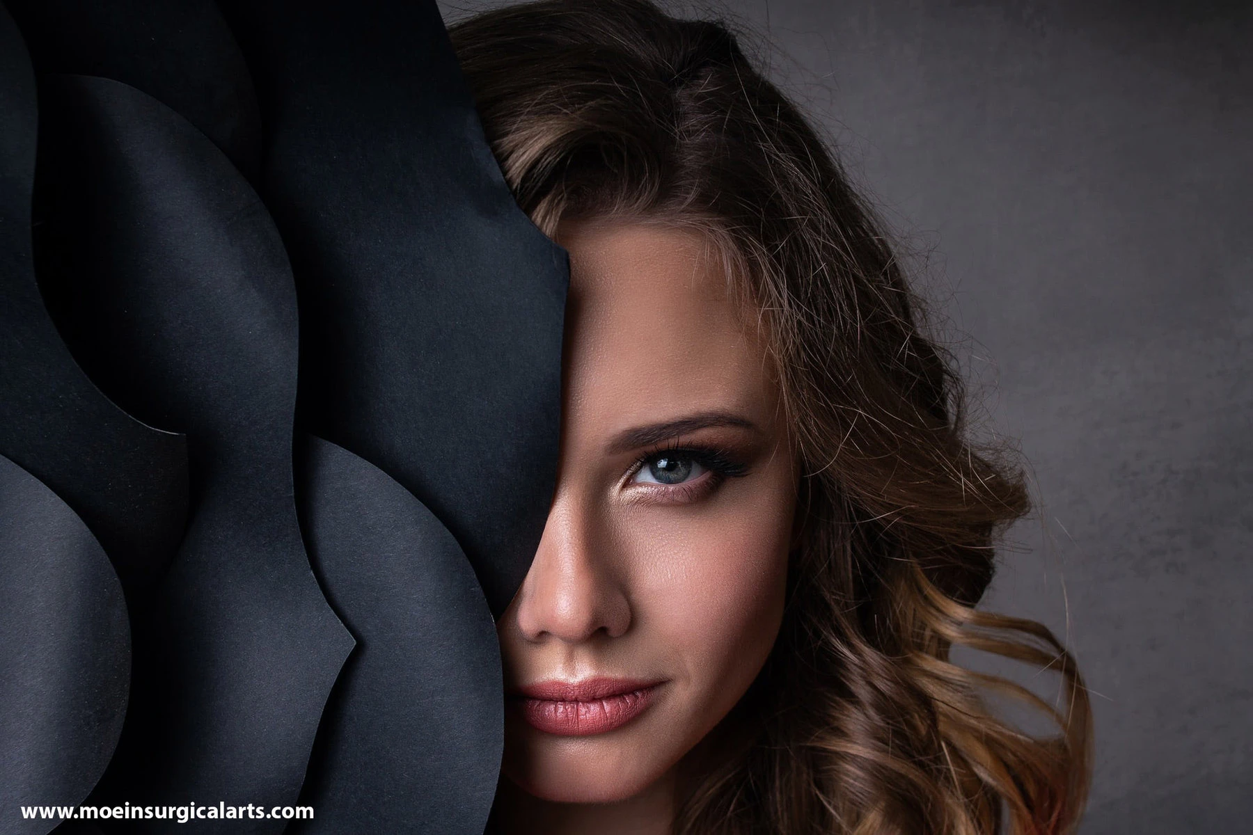 A young woman is hiding behind a black sheet of paper.