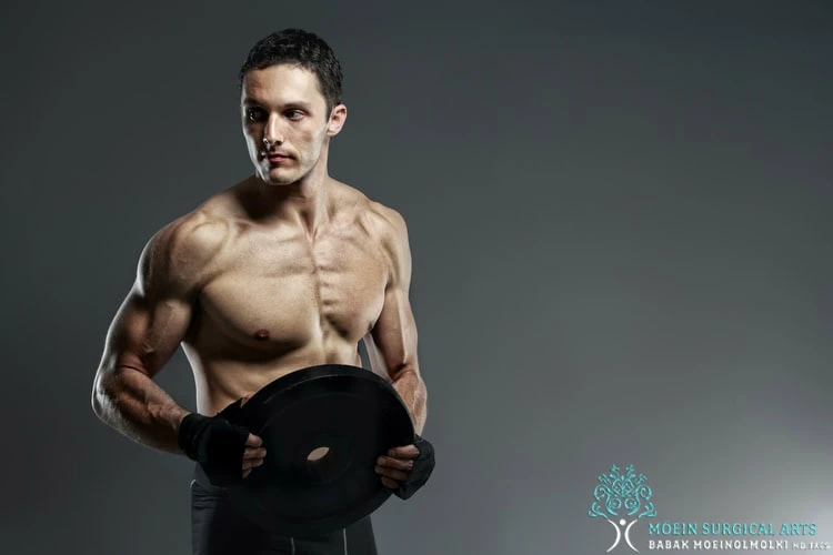 A man is posing with a dumbbell on a grey background.