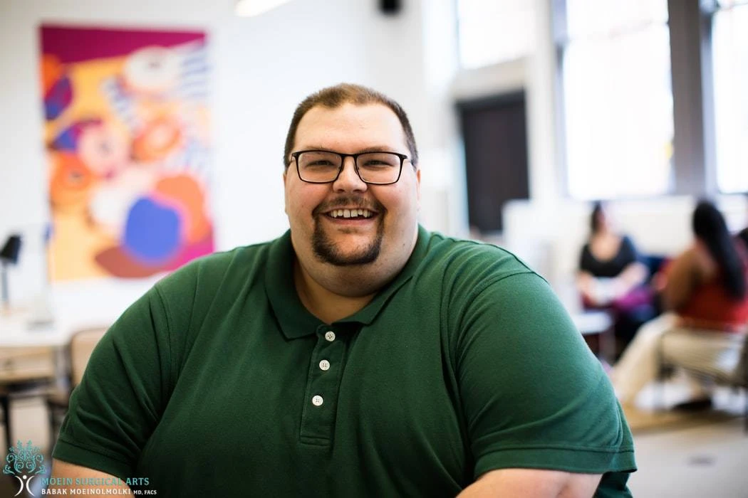 A man in a green shirt smiling in a classroom.